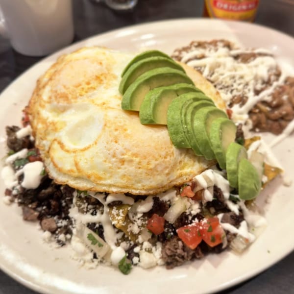 A plate of chilaquiles with two fried eggs, sliced avocado, and refried beans.