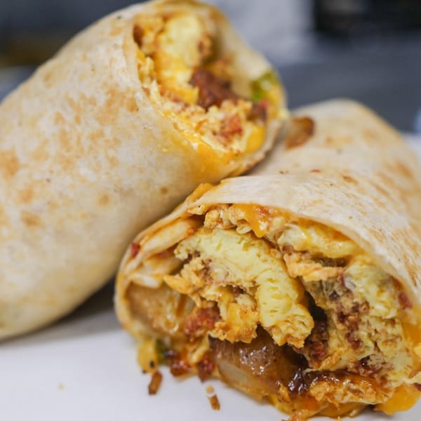 Two breakfast burritos, one cut in half, revealing eggs, cheese, and sausage inside.